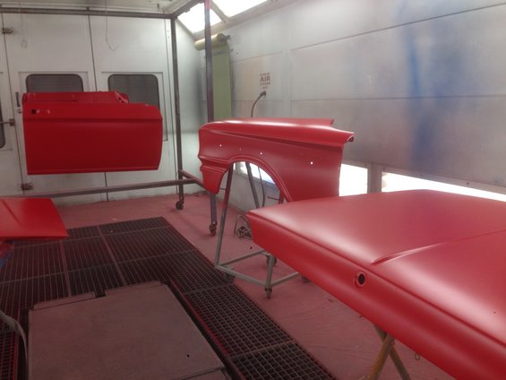 Red car door, fender, and hood in a paint booth