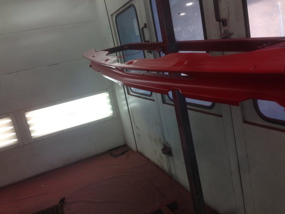 Red car bumper hanging in a paint booth