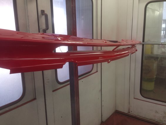 Red car fender section on a stand in a paint booth