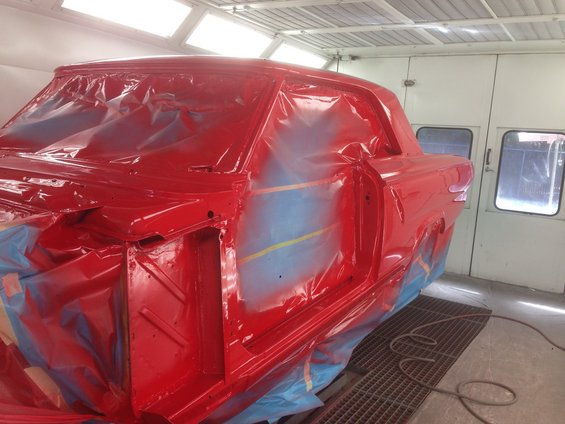 Car body covered in red plastic, being prepped for paint in a booth