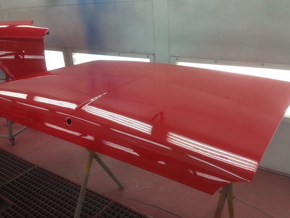 Red car hood with two prominent creases, resting on sawhorses in a paint booth