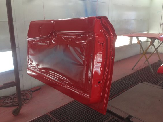 Red car door hanging in a paint booth