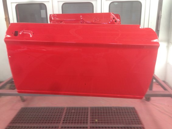 Two red car doors are drying in a paint booth. One door is in focus in the foreground