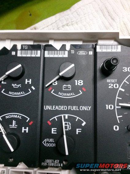 Car dashboard gauges with oil, battery, fuel, and temperature indicators. Part number visible