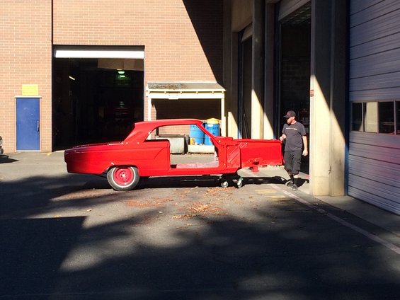 1964 Ford Fairlane body shell, red, on a red dolly outside a garage