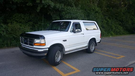 White Ford Bronco parked in a lot, front 3/4 view. Black bug deflector on hood