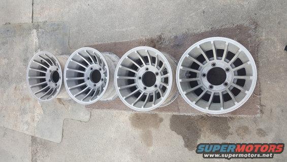 Four silver aluminum alloy wheels with a multi-spoke design are laid out on a concrete surface