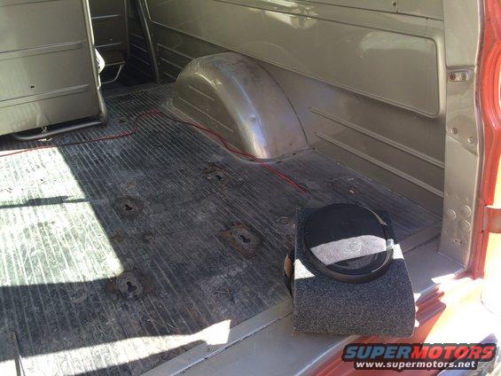 Interior cargo area of a van or truck, showing ribbed floor, wheel well, and a speaker box
