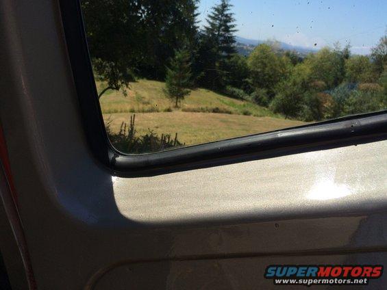 Interior view from a vehicle looking out the window at a grassy hill and trees