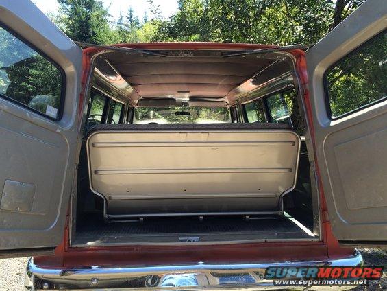 Rear view of a van with the back doors open, showing a folded-down seat and interior