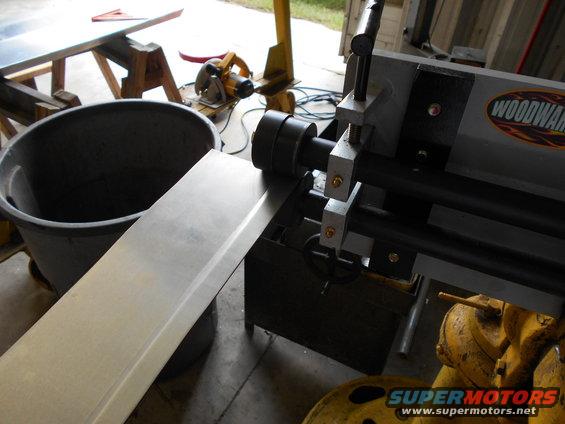 Metal sheet being fed into a Woodward roller machine, with a large bin and tools in background