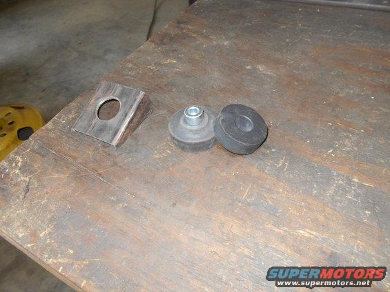 Metal bracket with a hole and two rubber mounts, one with a bolt, on a wooden surface