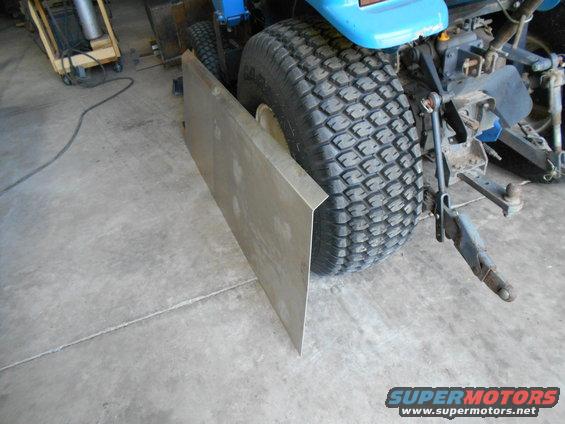 Rear tire of a blue lawn tractor with a metal plate attached to the side