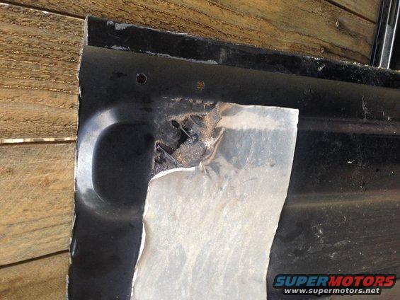 Damaged black metal panel with rust and torn silver material, against wooden planks