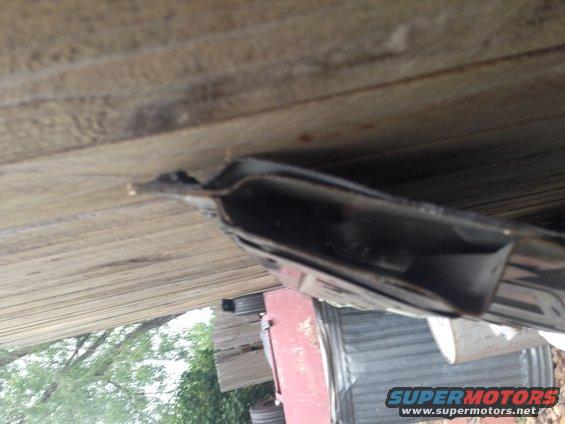 Close-up of a dark metal vehicle frame part against wooden planks