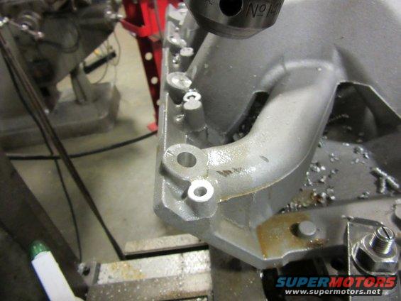 Close-up of an engine intake manifold being worked on with a drill press