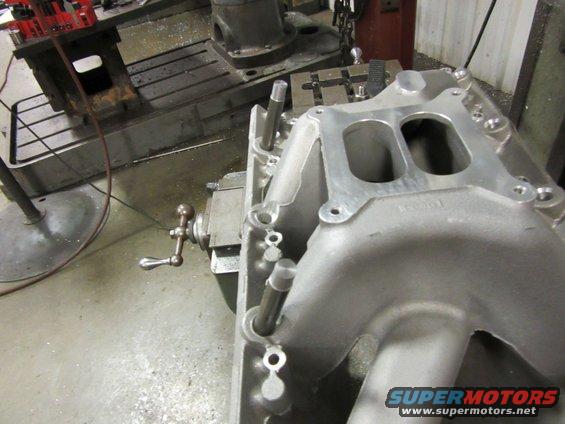Aluminum intake manifold with dual openings, on a workbench with machinery