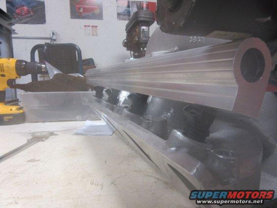 engine intake manifold on workbench with drill and caliper nearby