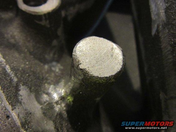 Close-up of a metal pin protruding from a dark, textured surface, possibly an engine block