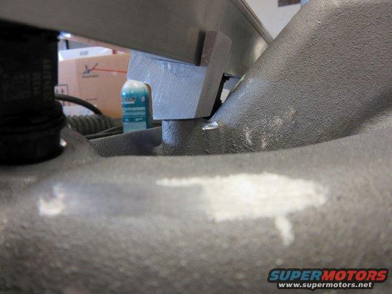 Close-up of a metal clamp on a textured engine component, with a bottle and box in the background