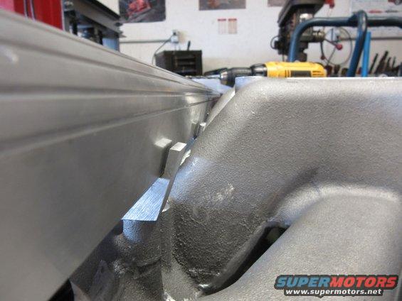 Close-up of an engine intake manifold with a metal rail above it. A yellow drill is visible in the background
