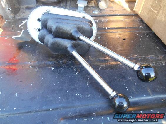 Two black shifter knobs on chrome levers, mounted on a metal plate with rubber boots