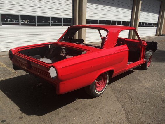 Red car body, likely a 1960s model, stripped down for restoration. Doors and roof are present, but interior and engine are missing