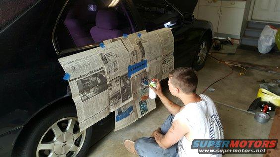 Guy spray painting a car door covered in newspaper. Purple seats visible inside