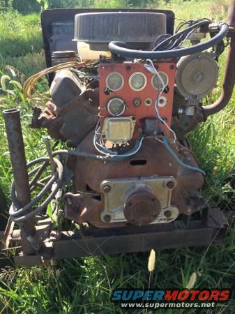 Rusty engine with gauges and wiring, mounted on a frame, outdoors in grass