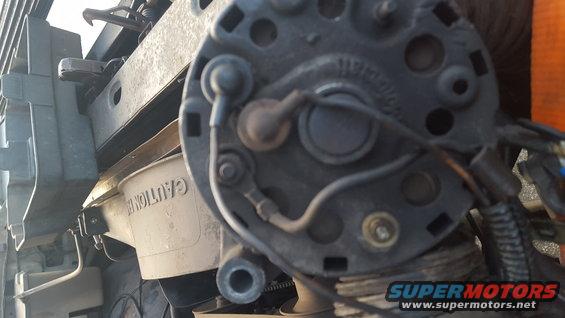 close-up of car alternator with wires and a white plastic reservoir labeled 'CAUTION'