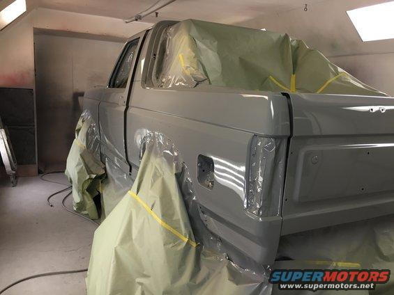 Gray Ford Bronco in paint booth, rear quarter view, covered in masking