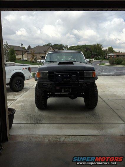 Black SUV with aftermarket bumper, hood scoop, and off-road lights, viewed from the front
