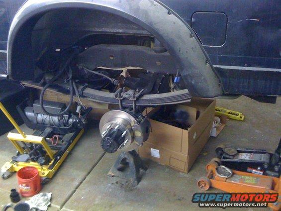 Rear axle and suspension parts on a vehicle being worked on, with a winch and jacks visible