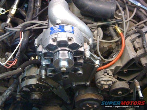 Close-up of a supercharger unit mounted on an engine, with various hoses and wires visible