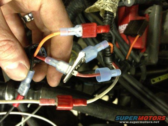 Close-up of a hand connecting wires with crimp connectors and a clip in a vehicle's engine bay