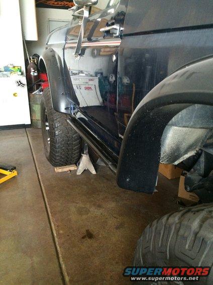 Black SUV side view, jack stands under rocker panel, large tires, reflection of garage interior in door