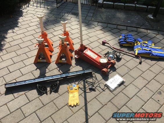 Car jack, jack stands, work gloves, LED light bar, and life vests laid out on a paved surface