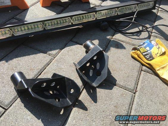 Two black metal welding brackets and a yellow welding glove next to a light bar