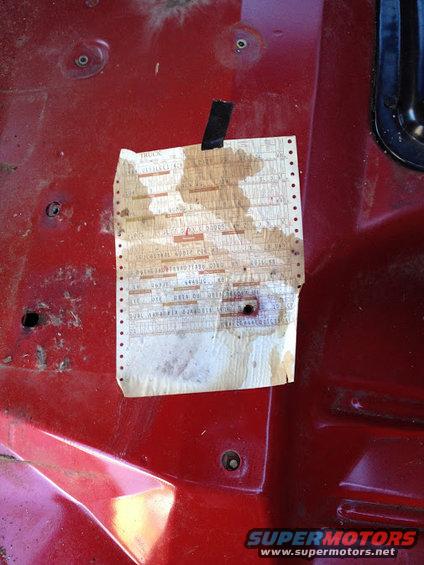 Tattered paper document taped to a red metal surface, possibly inside a vehicle