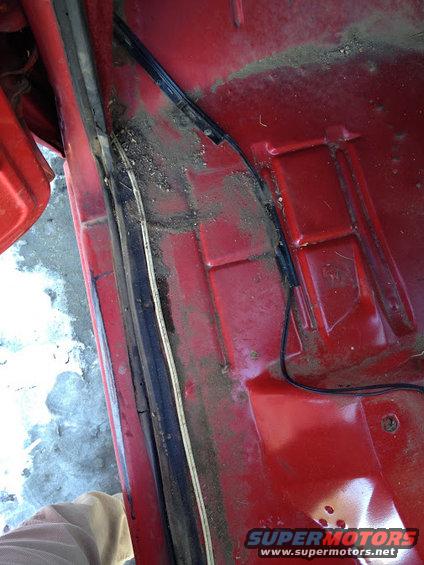 Close-up of red interior floor pan with dirt and wiring near door jamb