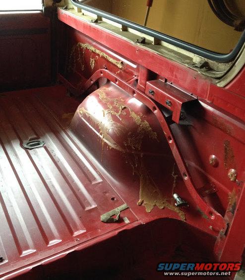 Interior of a red truck bed, showing the wheel well and some dried residue on the side panel