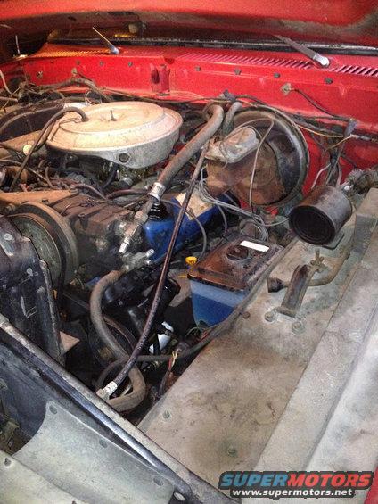 Engine bay with V8 engine, air cleaner, brake booster, and fluid reservoir. Red paint visible on firewall