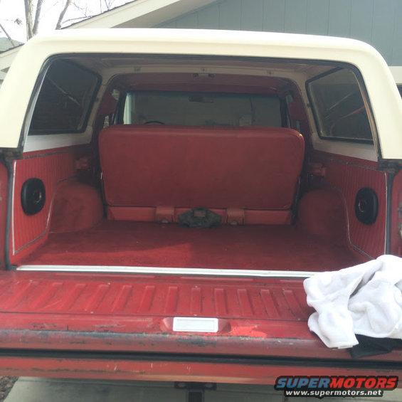 Red interior of a 1978 Ford Bronco with a folded rear seat and a white towel on the right