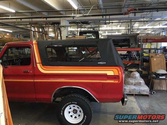 Side view of a red 1978 Ford Bronco with orange and yellow stripes and a black soft top, parked indoors