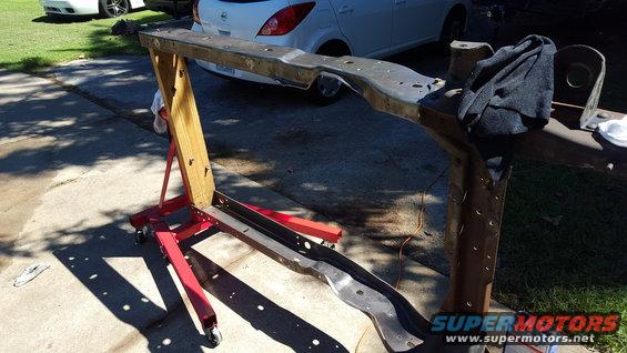 Vehicle frame on engine stand with two cars in background