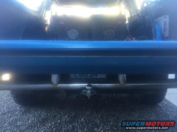 Rear view of a blue SUV showing a trailer hitch and two aftermarket speakers inside the cargo area. License plate reads LUU034