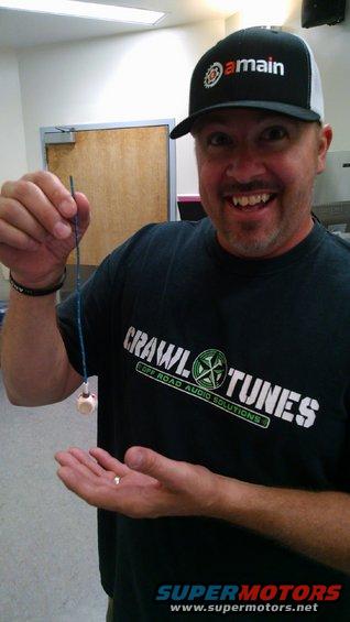 Man in a black t-shirt with 'Crawl Tunes' logo and a black cap with 'amain' logo, holding a small object