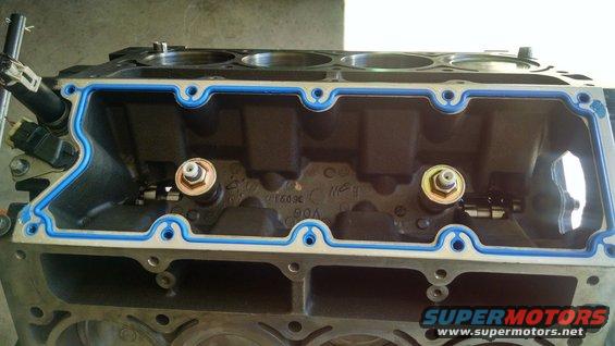 Engine block with blue gasket installed. Two bolts with sensors are visible inside