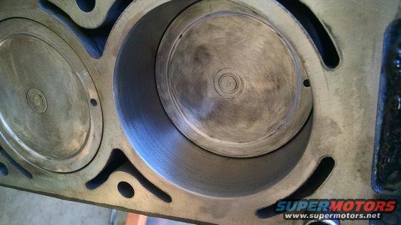 Close-up of two engine cylinders, one with a piston visible inside. The metal shows signs of wear