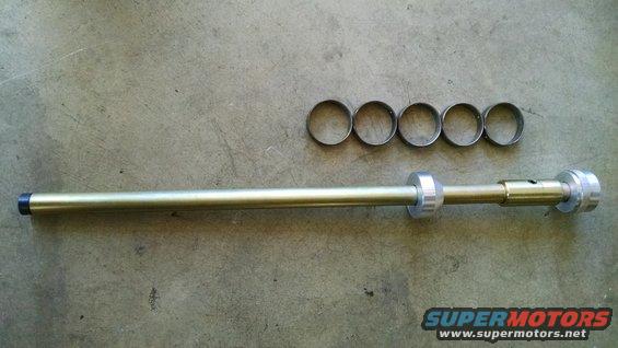 Metal tool with a long shaft, adjustable rings, and a cap, next to five loose rings on a concrete surface